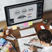 Secretos para crera un diseño gráfico que enamora Diseñador gráfico bocetando y enfrente de su computadora con logos